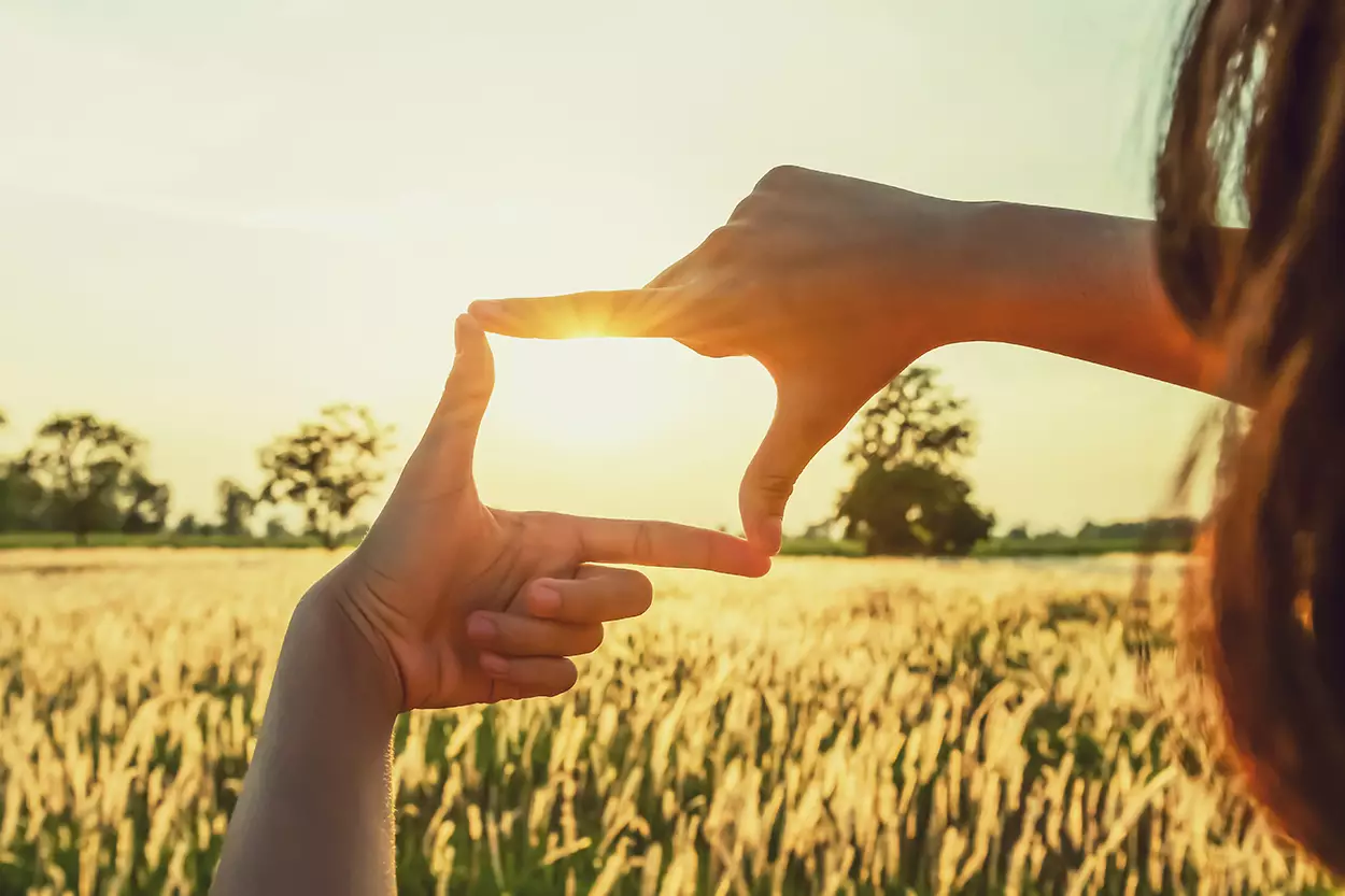 Photo of a person putting their thumb and index fingers from both hands into a square shape and holding it up to the sky as the sunrises, like they're looking through a window.